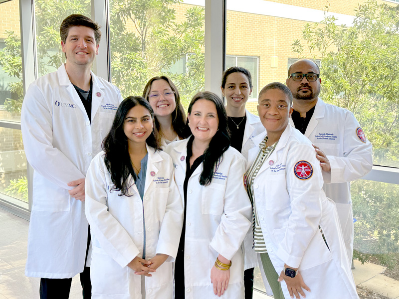 A group of clinical anatomy graduate students in their white lab coats smile.